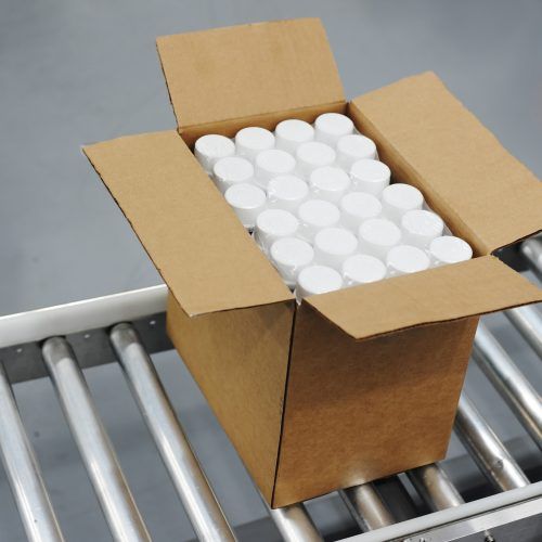 Shot of single, unsealed box traveling on a conveyor in a manufacturing facility. Plastic bottles are visible inside the box.